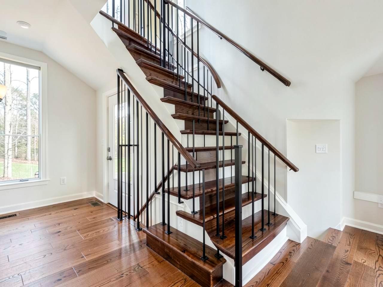 Refinished dark wood staircase with slender black railing spindles beside hardwood flooring